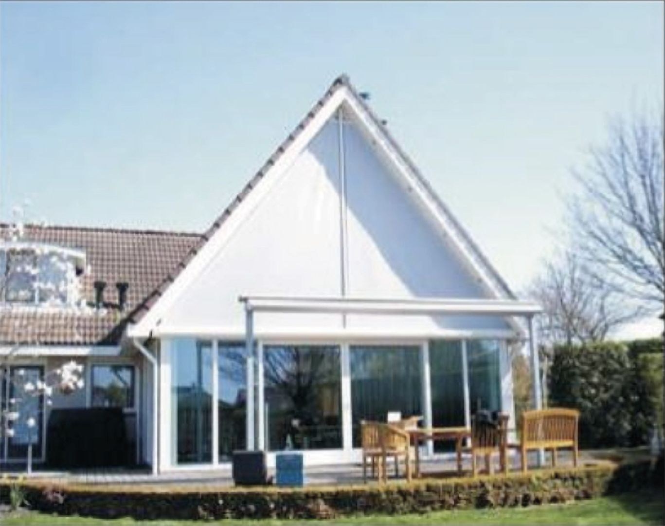 Modernes Einfamilienhaus mit großem dreieckigem Giebelfenster und Terrasse mit Gartenmöbeln.